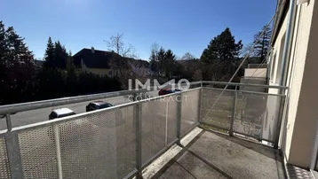 Sonniger Balkon mit Metallgeländer und Ausblick auf Bäume und die umliegende Wohngegend.