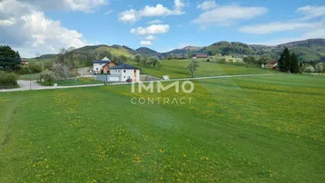 Weitläufige Landschaft mit einem modernen Wohnhaus inmitten grüner Wiesen und Hügel.
