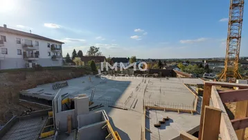 Baustelle mit bereits gegossener Bodenplatte und vorbereiteter Bewehrung für den weiteren Baufortschritt unter blauem Himmel.