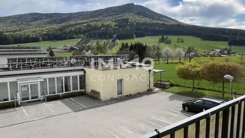 Weitblick vom Balkon über einen Parkplatz und Gebäude auf die umliegende Berglandschaft.