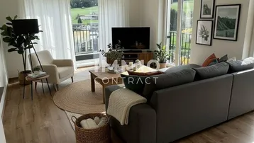 Gemütliches Wohnzimmer mit großem Sofa, Blick ins Grüne und auf die Berge durch große Fenster.