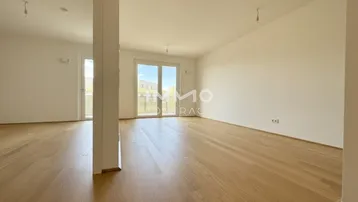 Helles, leeres Zimmer mit Parkettboden und Zugang zu einem Balkon, ideal für einen offenen Wohnbereich.