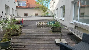 Geräumige Holzterrasse mit Sitzgelegenheiten und Pflanzenkübeln zwischen den Gebäuden.