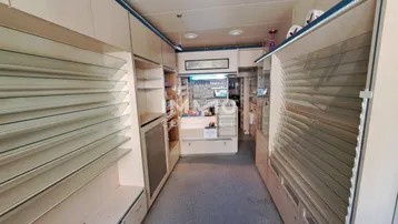 Geräumiger Ladenbereich mit langen Regalen, einem Verkaufstresen im Hintergrund und Teppichboden.