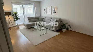 Virtuell inszeniertes Wohnzimmer mit modernem Sofa, Laminatboden und Zugang zum Balkon.