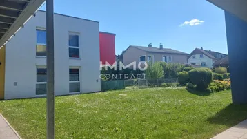 Blick auf das Gebäude mit einer großen Rasenfläche im Vordergrund und weiteren Häusern im Hintergrund.