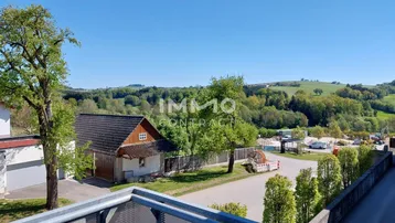 Weitläufiger Blick vom Balkon auf die grüne Hügellandschaft und umliegende Natur.