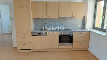 Helle Einbauküche mit Holzfronten, modernen Geräten und Fenster mit Tageslicht.