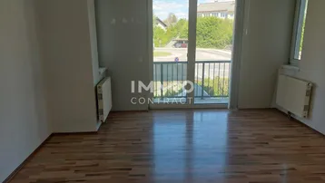 Helles, leeres Wohnzimmer mit Laminatboden, Heizkörpern und Zugang zu einem französischen Balkon.