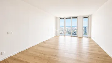 Helles, leeres Wohnzimmer mit Holzboden und großen Fenstern mit Stadtblick.