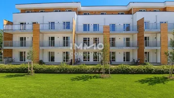 Moderne Wohnanlage mit weißen Fassaden, Holzverkleidung und Balkonen, umgeben von Grünflächen.