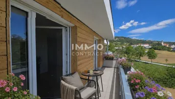 Möblierter Balkon mit Holzwänden, Blumenkästen und weitem Blick ins Grüne.