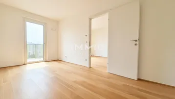 Helles Zimmer mit Holzboden und Zugang zu einem Balkon, ideal als Wohn- oder Schlafbereich.