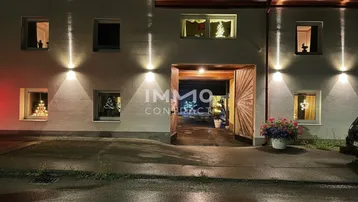 Beleuchtete Hausfassade bei Nacht mit festlicher Dekoration in den Fenstern und einer großen Holztür.