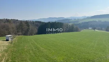 Panoramablick über weite grüne Felder und Wälder mit hügeliger Landschaft im Hintergrund bei klarem Wetter.