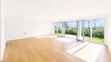 Helles, leeres Wohnzimmer mit Holzboden und großen Fenstern, die Zugang zum Garten bieten.