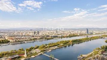 Panoramablick über die Stadt Wien mit der Donau und umliegenden Gebäuden unter blauem Himmel.