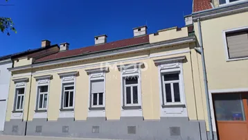Gelbe Fassade eines Altbaus mit mehreren Fenstern und Rollläden unter blauem Himmel.