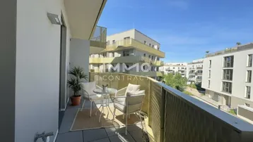 Möblierter Balkon mit Fliesenboden und Blick auf moderne Wohngebäude unter blauem Himmel.