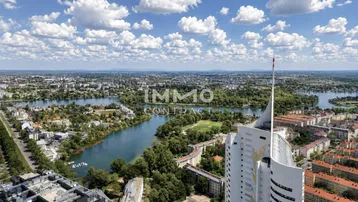 Panoramablick auf die Stadt mit Fluss, grünen Ufern und markanten Hochhäusern unter blauem Himmel.