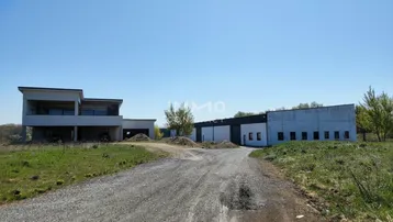Blick auf das Anwesen mit einem modernen Wohngebäude und einer angrenzenden Industriehalle unter blauem Himmel.