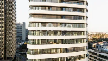 Moderne Hochhausfassade mit geschwungenen Balkonen und großen Fenstern in urbaner Umgebung.