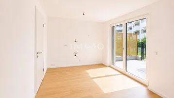 Helles, leeres Zimmer mit Holzboden und Zugang zu einer Terrasse, ideal als Wohn- oder Schlafzimmer.