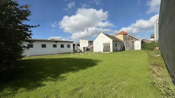 Großer Gartenbereich mit Rasenfläche und älteren Nebengebäuden unter blauem Himmel.