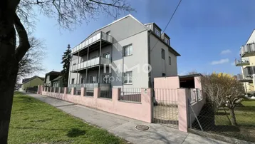 Mehrstöckiges Wohngebäude mit moderner grauer Fassade, mehreren Balkonen und einem rosa Zaun.