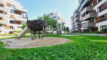 Moderner Spielplatz mit Rutsche und Klettergerüst zwischen Wohngebäuden, umgeben von Grünflächen.