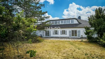 Charmantes Haus mit einzigartigem Dach und vielen Fenstern, umgeben von einem weitläufigen Garten.