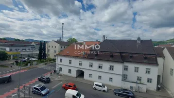 Blick von oben auf ein historisches Gebäude mit rotem Dach und die umliegende Stadtlandschaft mit Straßenverkehr.