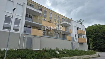 Moderne Wohnanlage mit mehreren Balkonen unter bewölktem Himmel und grüner Umgebung.