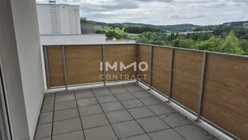 Geräumiger Balkon mit Fliesenboden und Holzverkleidung, bietet einen weiten Blick ins Grüne.