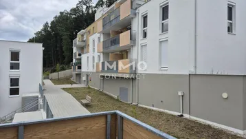 Modernes Mehrfamilienhaus mit Balkonen und Zugangswegen in einer grünen Umgebung.
