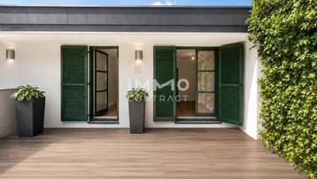 Geräumige Terrasse mit Holzplankenboden, grünen Fensterläden und üppiger Begrünung an der Wand.