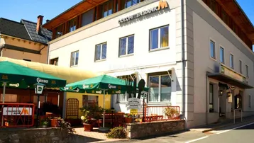Gebäude mit Restaurant-Terrasse, grünen Sonnenschirmen und Blick auf die Straße.