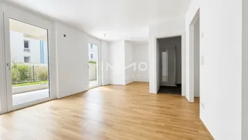 Helles, leeres Zimmer mit Parkettboden, weißen Wänden und Zugang zu einer Terrasse.