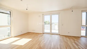 Heller, leerer Wohnraum mit modernem Holzboden, großen Fenstern und Zugang zu einem Balkon.