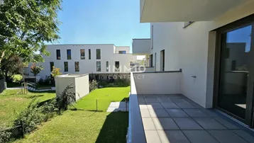 Helle Terrasse mit Fliesenboden und Blick auf die grüne Gartenanlage und moderne Gebäude.