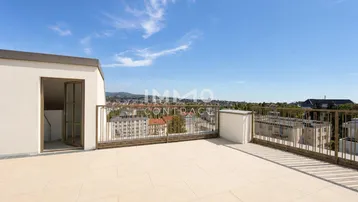 Große Dachterrasse mit Fliesenboden und weitem Blick über die Stadt und Berge.