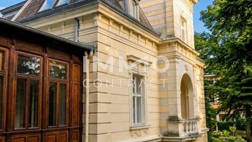 Historische Villa mit Mansarddach und dekorativen Elementen, umgeben von einem gepflegten Garten.