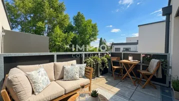 Gemütlicher Balkon mit bequemen Gartenmöbeln, Pflanzen und Blick ins Grüne unter blauem Himmel.