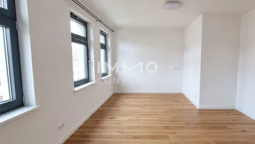 Helles Zimmer mit Holzboden und mehreren Fenstern, ideal als Wohn- oder Schlafbereich.