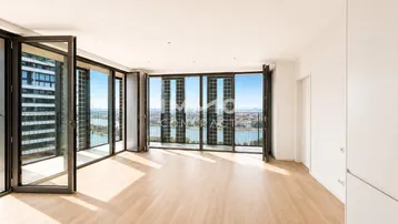 Helles, modernes Wohnzimmer mit Holzboden und raumhohen Fenstern, die einen weiten Blick auf den Fluss und die Stadt bieten.