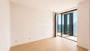 Heller Raum mit Holzboden und großen Glasfronten, die zu einem Balkon mit Stadtblick führen.
