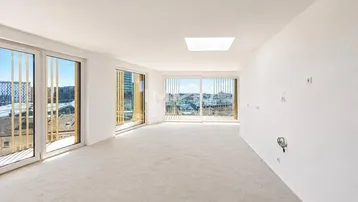 Helles, leeres Zimmer mit großen Fenstern, Teppichboden und weitem Stadtblick.