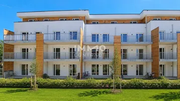 Moderne Wohnanlage mit weißer Fassade, Holzverkleidung und Balkonen, umgeben von Grünflächen.