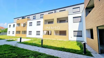 Moderne Wohnanlage mit weißer und holzverkleideter Fassade sowie kleinen Grünflächen davor.