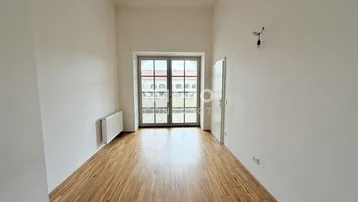 Heller Raum mit Holzboden, weißen Wänden und Zugang zu einem französischen Balkon mit Ausblick.